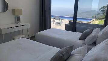 A hotel room with two beds, a desk, a chair, and a view of the ocean.