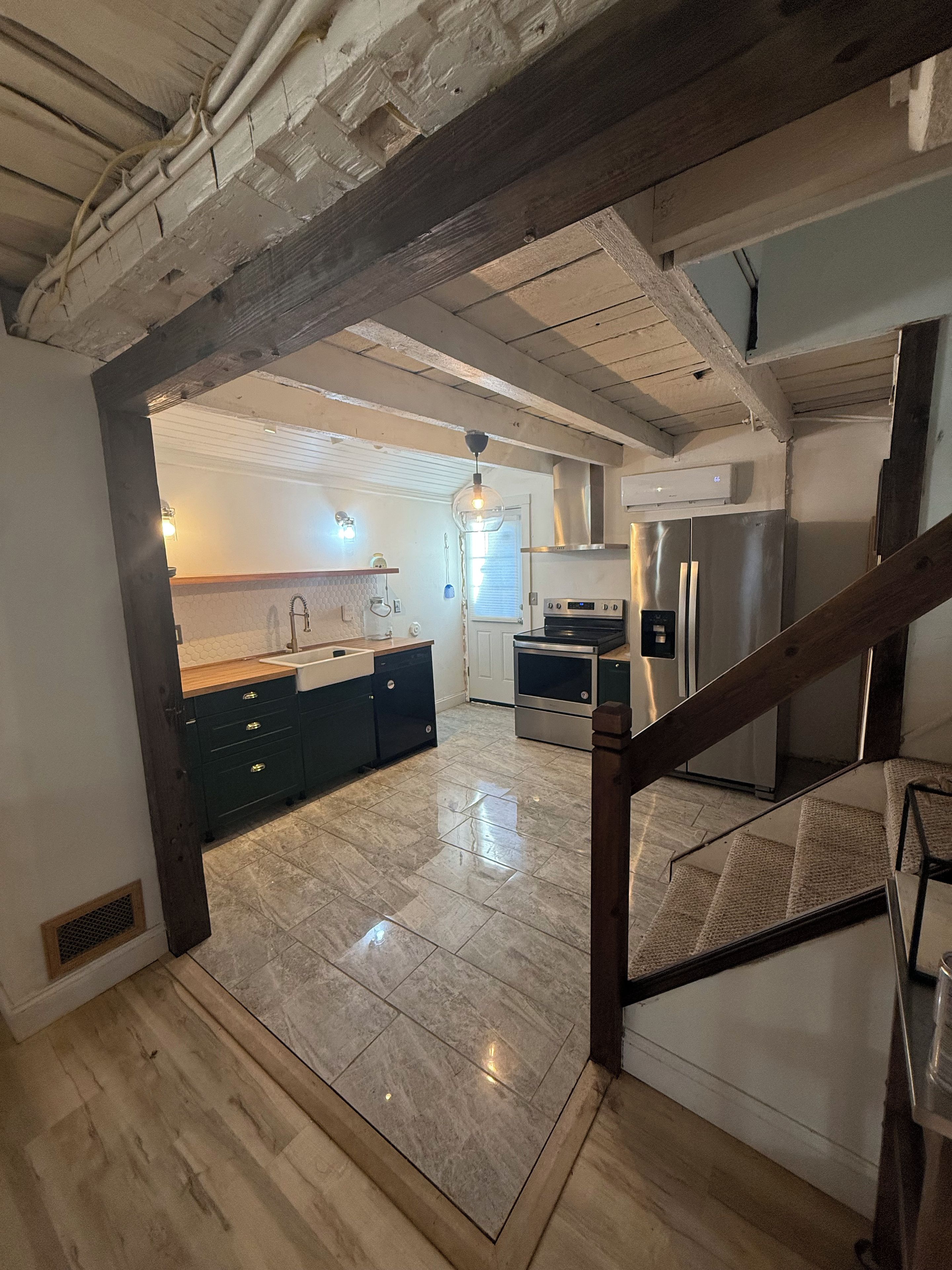 A modern kitchen with a central island, stainless steel appliances, and a wooden staircase.