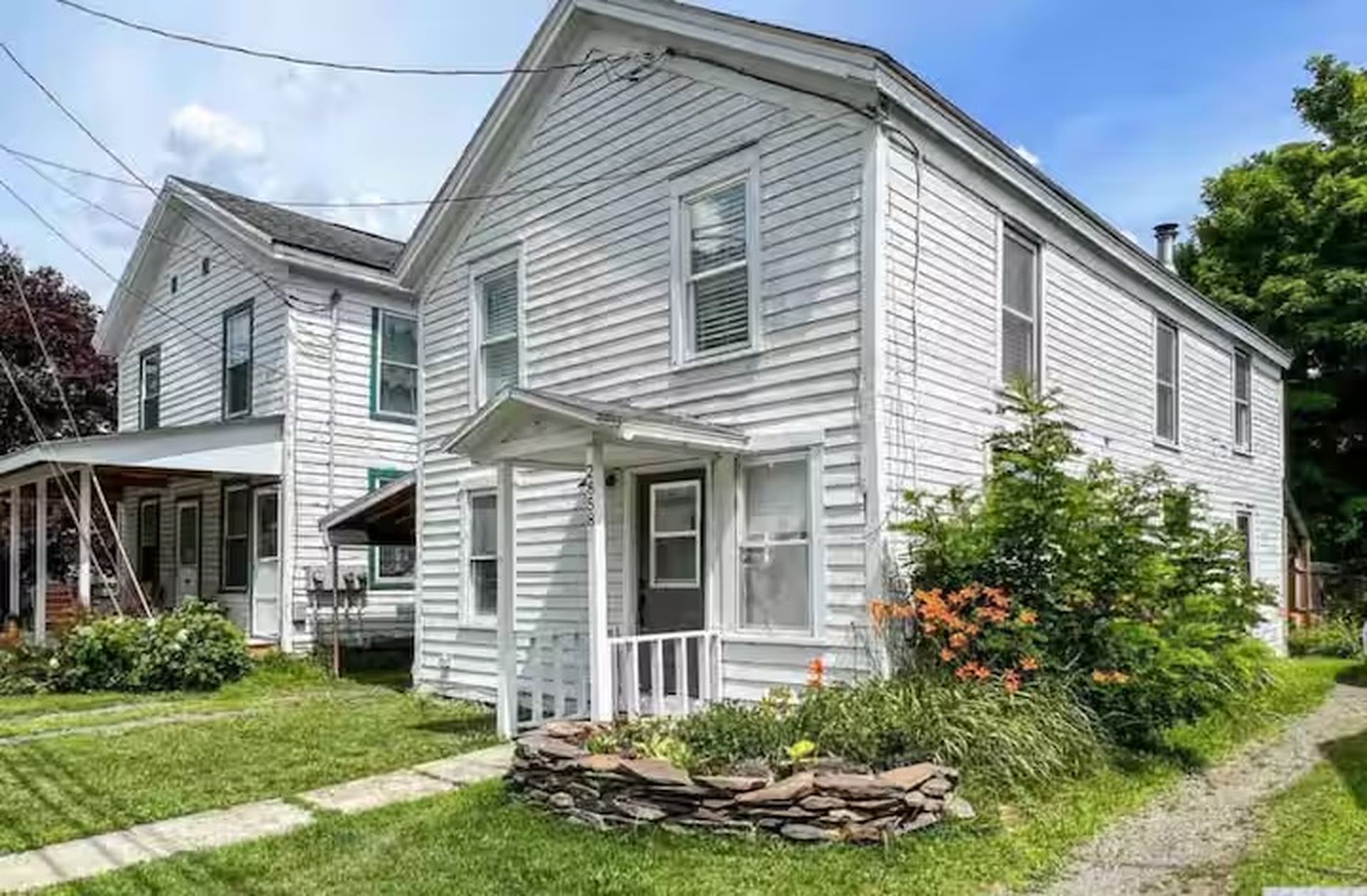 Une maison à deux étages avec un porche à l’avant et des fondations en pierre.