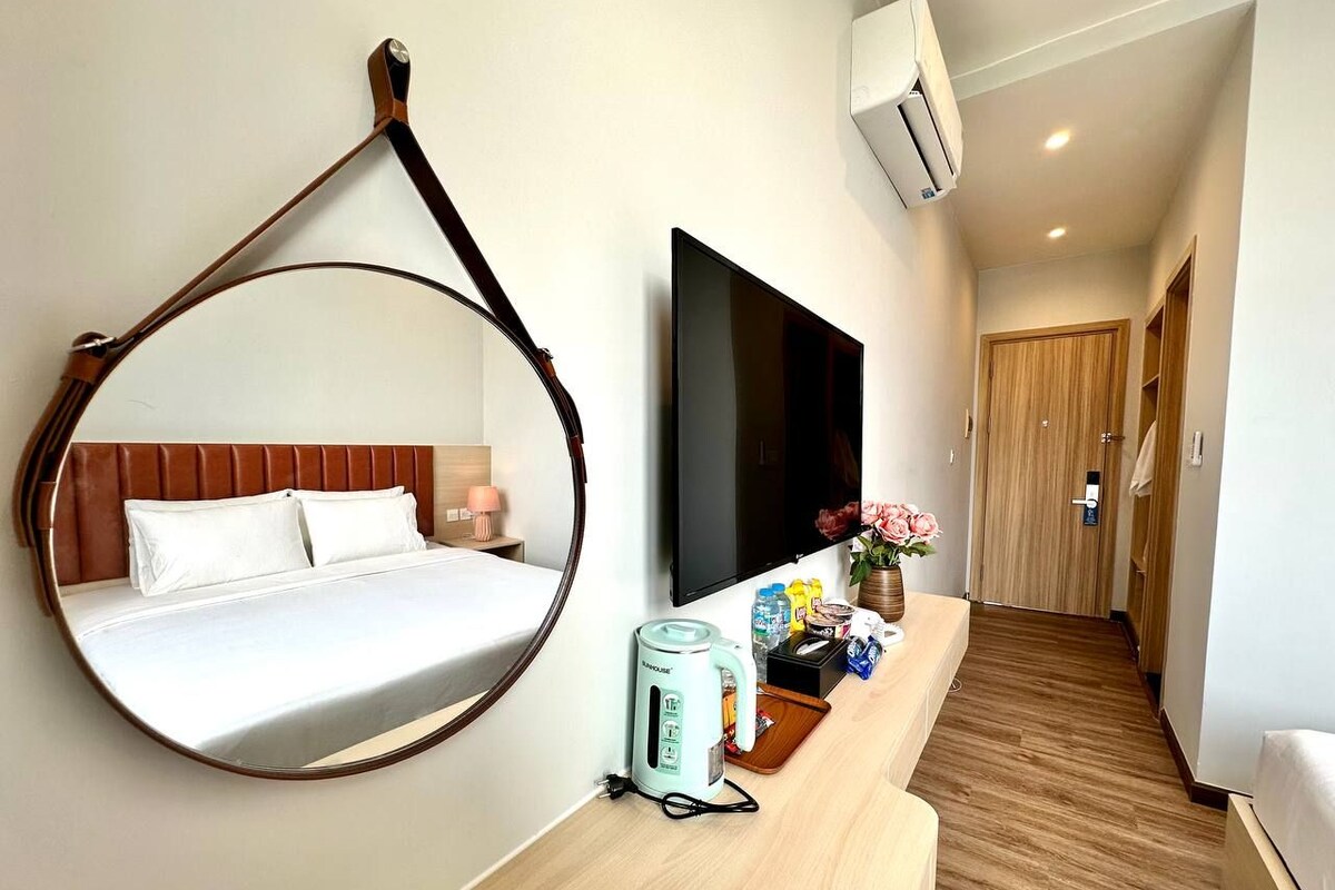 Quarto de hotel com cama, televisão, cafeteira e espelho.