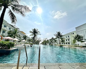 Una piscina con cielo despejado, palmeras y edificios al fondo.
