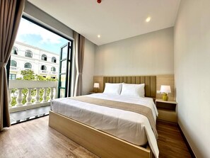 Habitación de hotel con una cama grande, dos mesitas de noche con lámparas, vista a un edificio por una ventana y un balcón con barandilla.