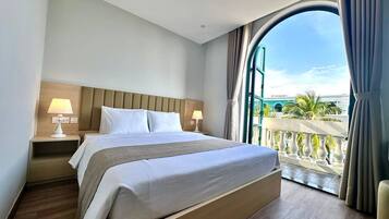 A hotel room with a large bed, a nightstand, a window with curtains, and a view of palm trees.