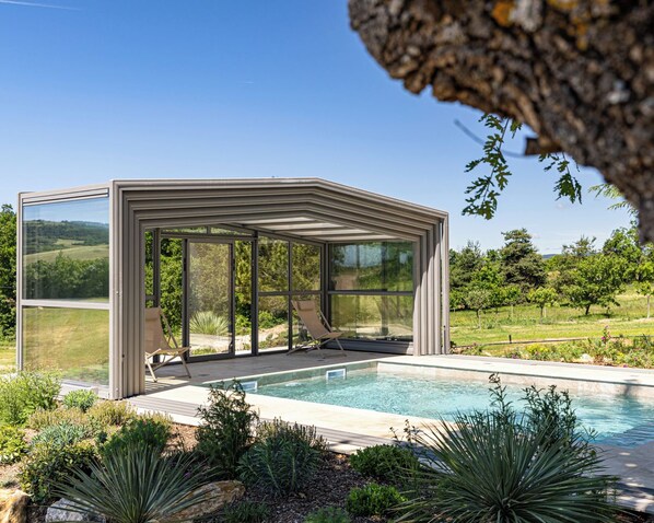 A modern outdoor pool area with a glass enclosure, surrounded by lush greenery and a clear view of the countryside. - Vrbo Property (Sault)