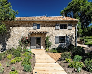 A stone house with a tiled roof, a wooden pathway leading to the entrance, and a garden with various plants. - Vrbo Property (Sault)