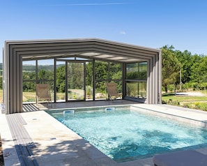 A covered swimming pool with clear blue water, surrounded by a deck with lounge chairs, and a view of a green landscape. - Vrbo Property (Sault)