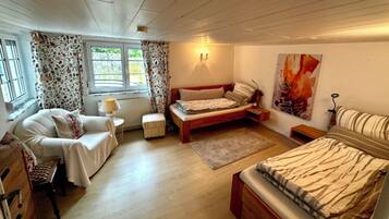 Ein Schlafzimmer mit Bett, Stuhl, Nachttisch, Lampe, Heizkörper und einem Fenster mit Vorhängen.