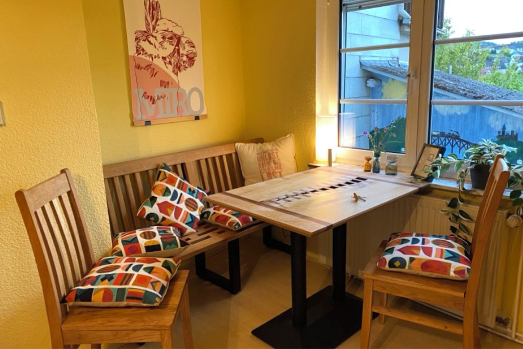 Ein Zimmer mit einer Holzbank, einem Tisch und Stühlen mit bunten Kissen.