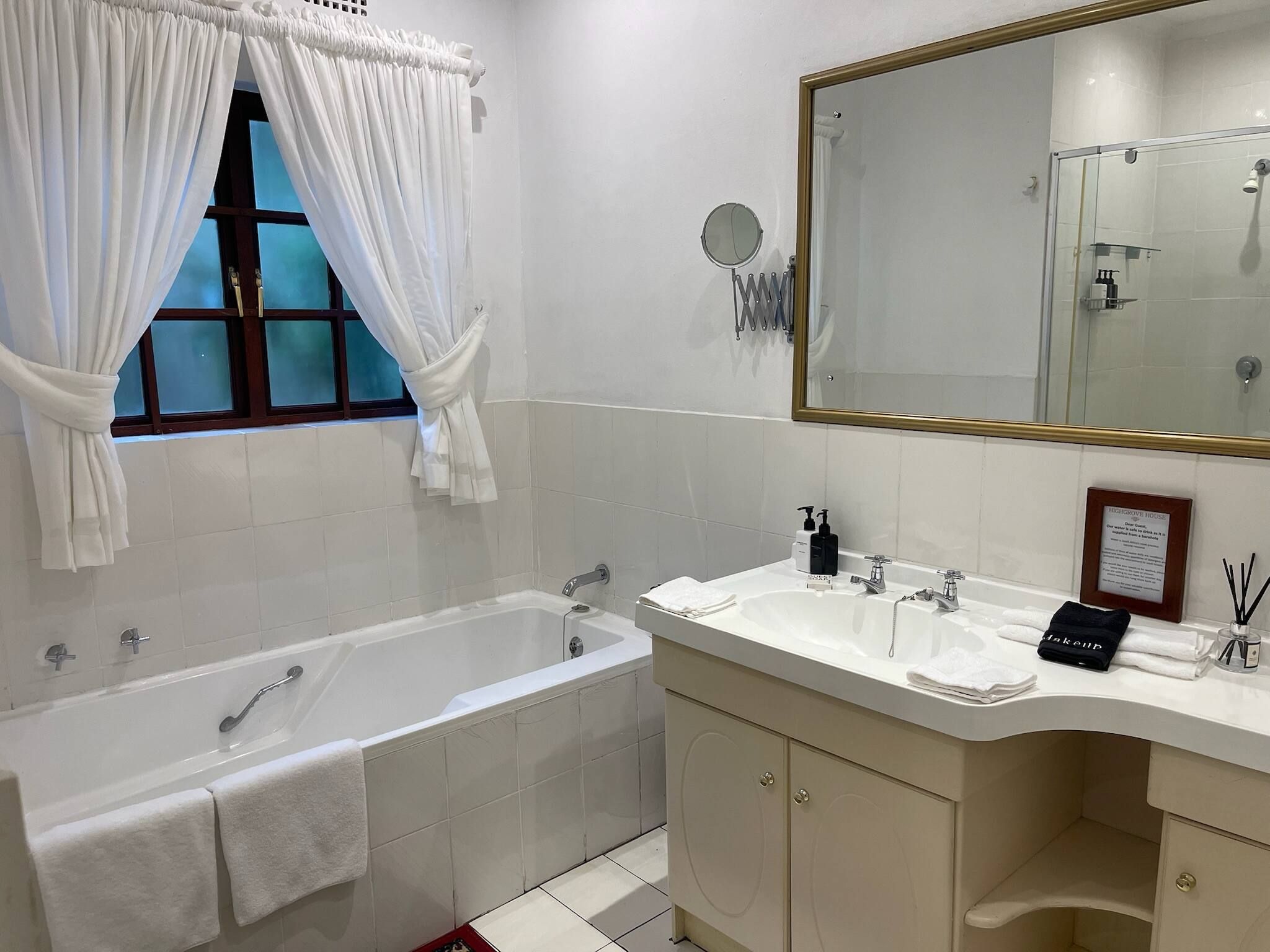 Un baño con bañera, dos lavamanos, un espejo grande y una ventana con cortinas.