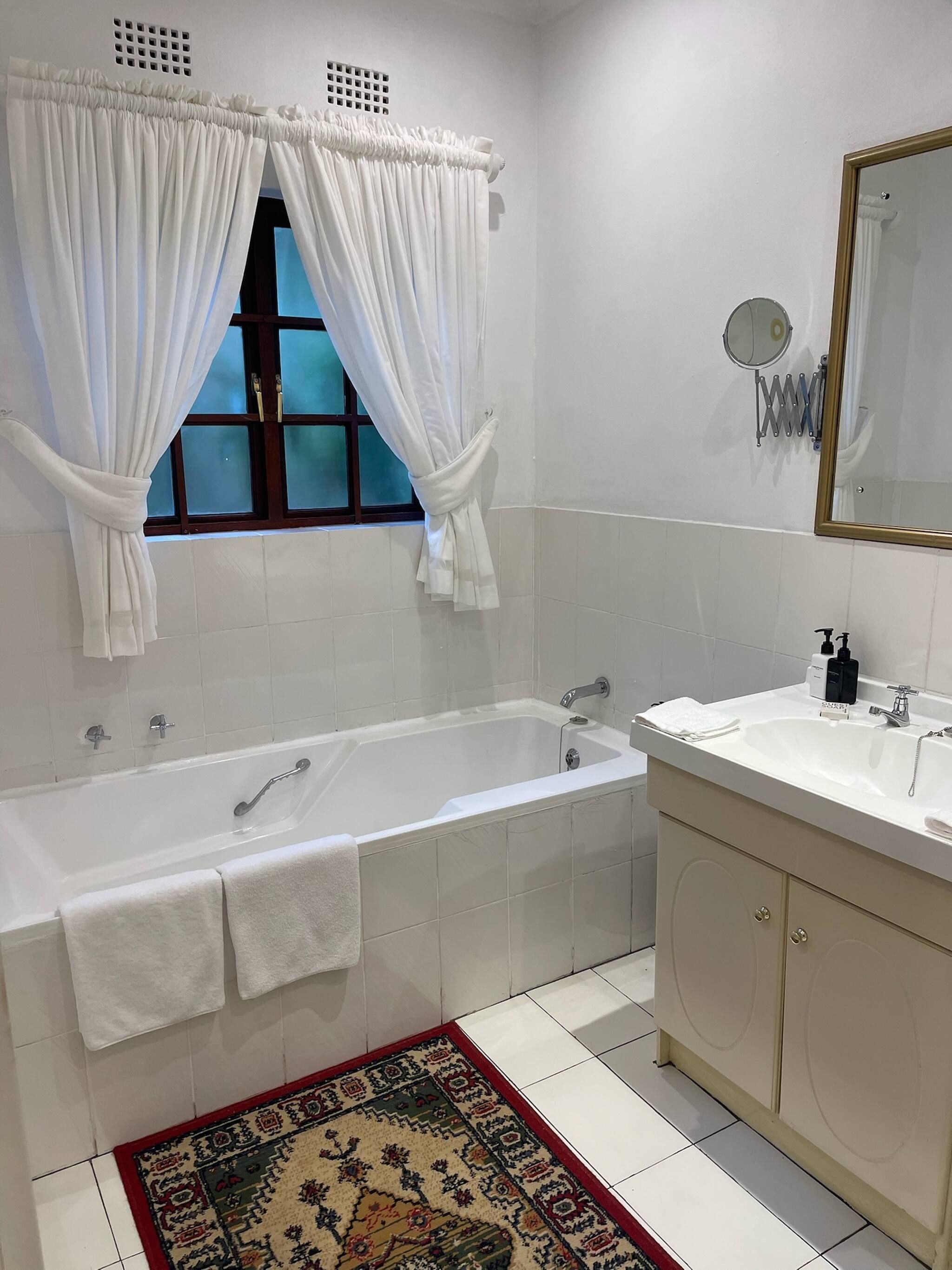 Une salle de bain avec une baignoire, un lavabo, un miroir et une fenêtre avec des rideaux.