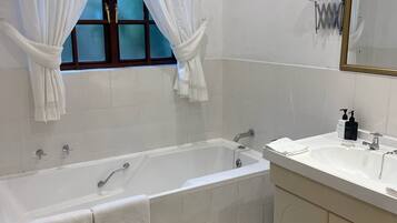 Une salle de bain avec une baignoire, un lavabo, un miroir et une fenêtre avec des rideaux.
