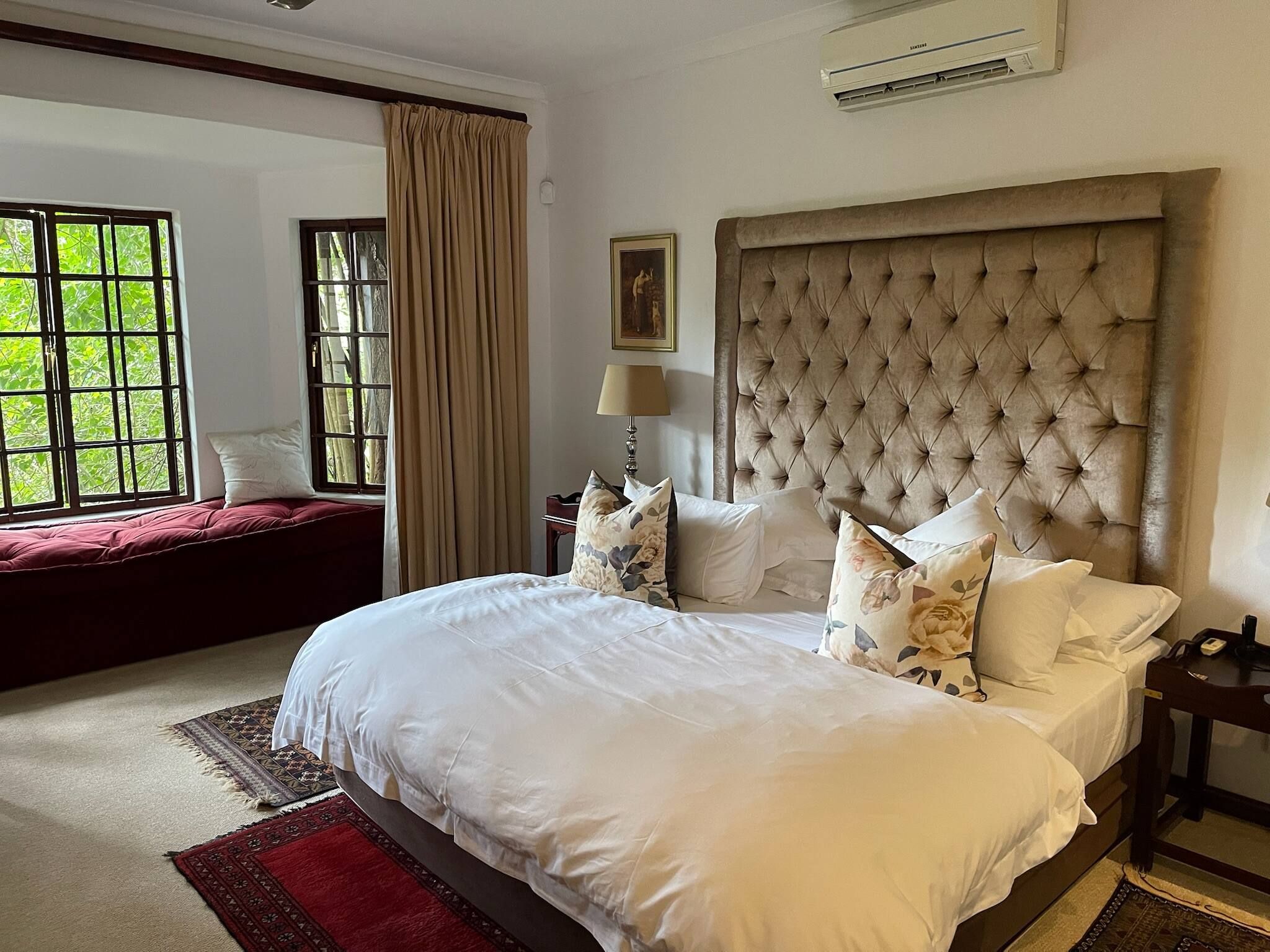 Une chambre d’hôtel avec un grand lit, une fenêtre avec des rideaux, une table de chevet avec une lampe et un appareil de climatisation.