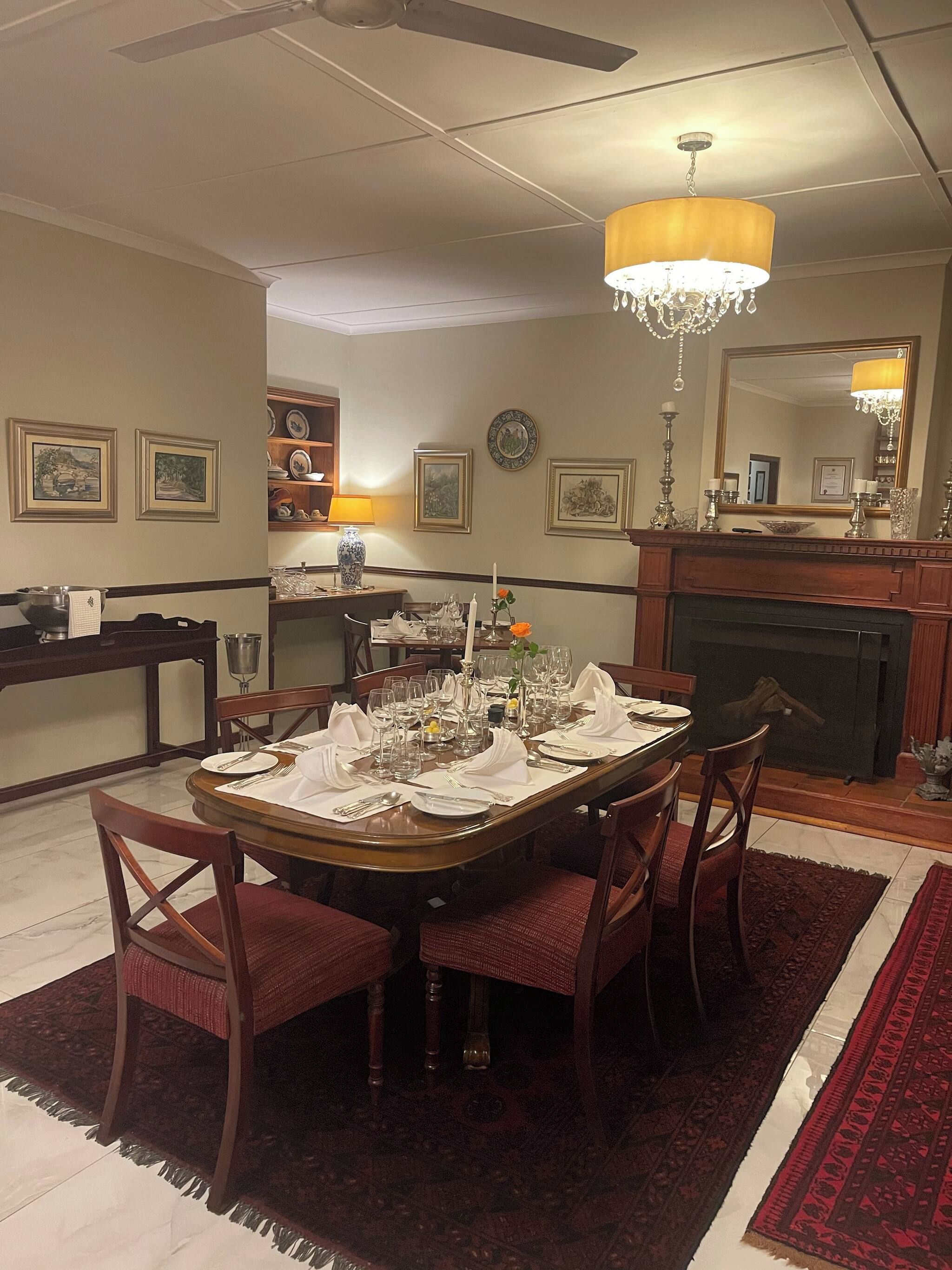 Une salle à manger avec une table ronde dressée pour un repas, entourée de chaises, d’un lustre et d’œuvres d’art encadrées accrochées aux murs.