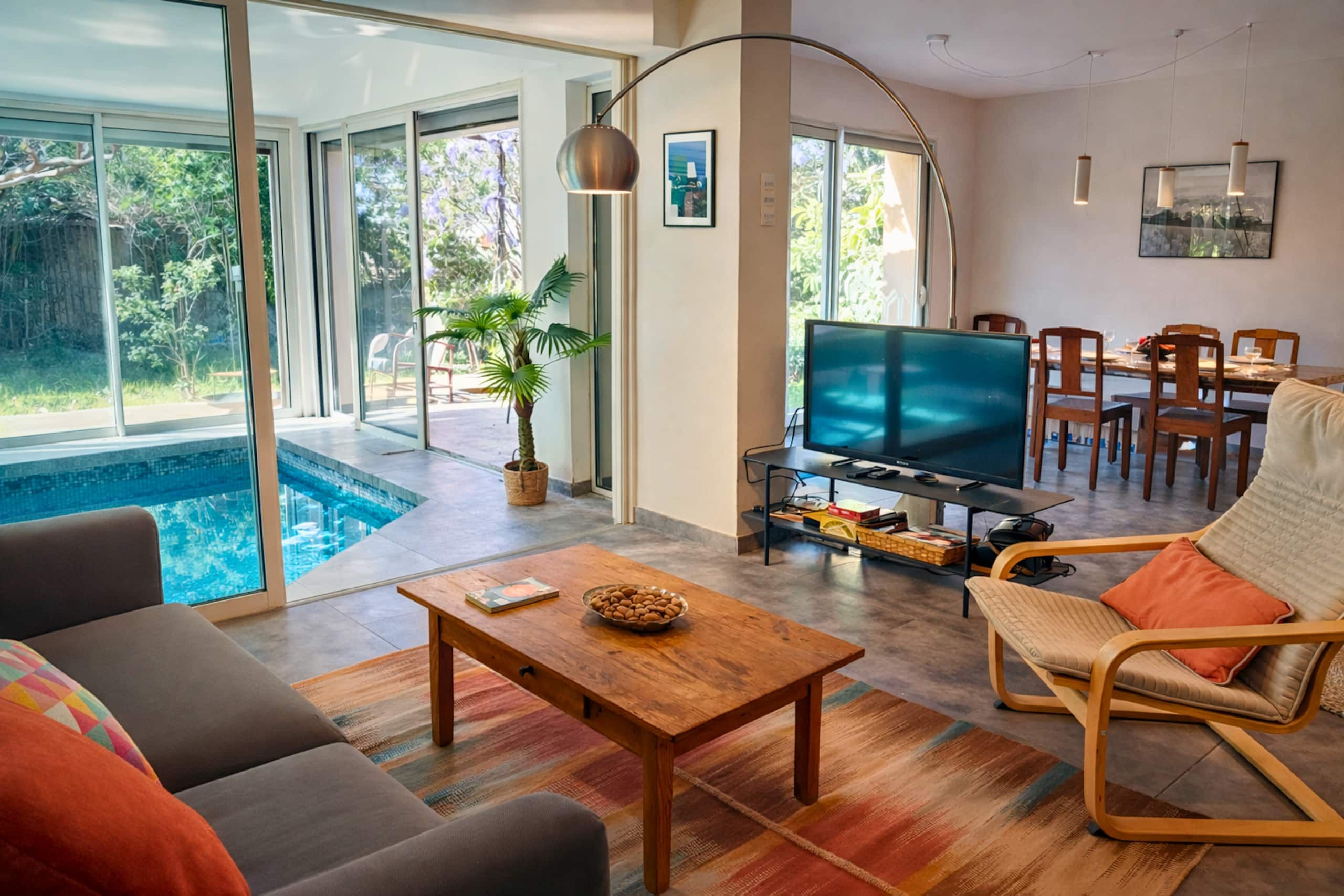 Ein modernes Wohnzimmer mit Pool, Fernseher und Essbereich.