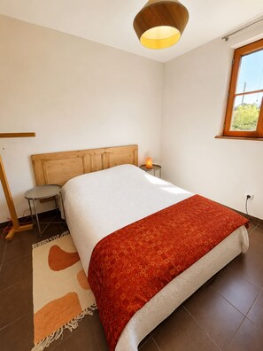 Un dormitorio con cama, mesita de noche, lámpara y ventana.