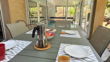 A dining table with a metal coffee pot, a glass of juice, and a bowl of fruit.