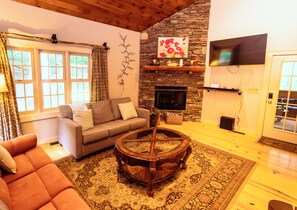 A cozy living room with a stone fireplace, a comfortable sofa, a coffee table, and a television mounted on the wall. - Cozy 4-bedroom house in tranquil Beech Mountain with AC And Hot Tub. (Beech Mountain)