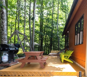 A wooden deck with picnic tables and chairs, surrounded by tall trees.
