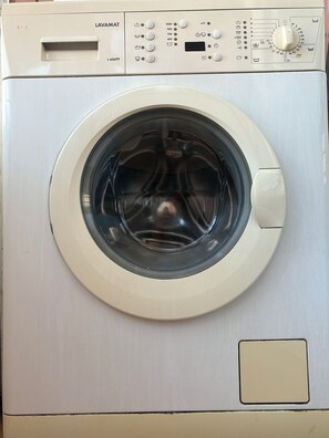 A front view of a white front-loading washing machine with a control panel and a circular door. - Vrbo Property (Unknown)