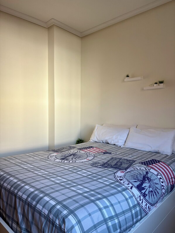 A bedroom with a bed, white pillows, a checkered bedspread, and two wall-mounted shelves with plants. - Vrbo Property (Unknown)