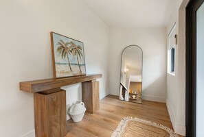 A hallway with a wooden console table, a painting of palm trees, a mirror, and a woven rug. - Our Miami House - Cozy 3BR Near Design District & Wynwood (Miami)