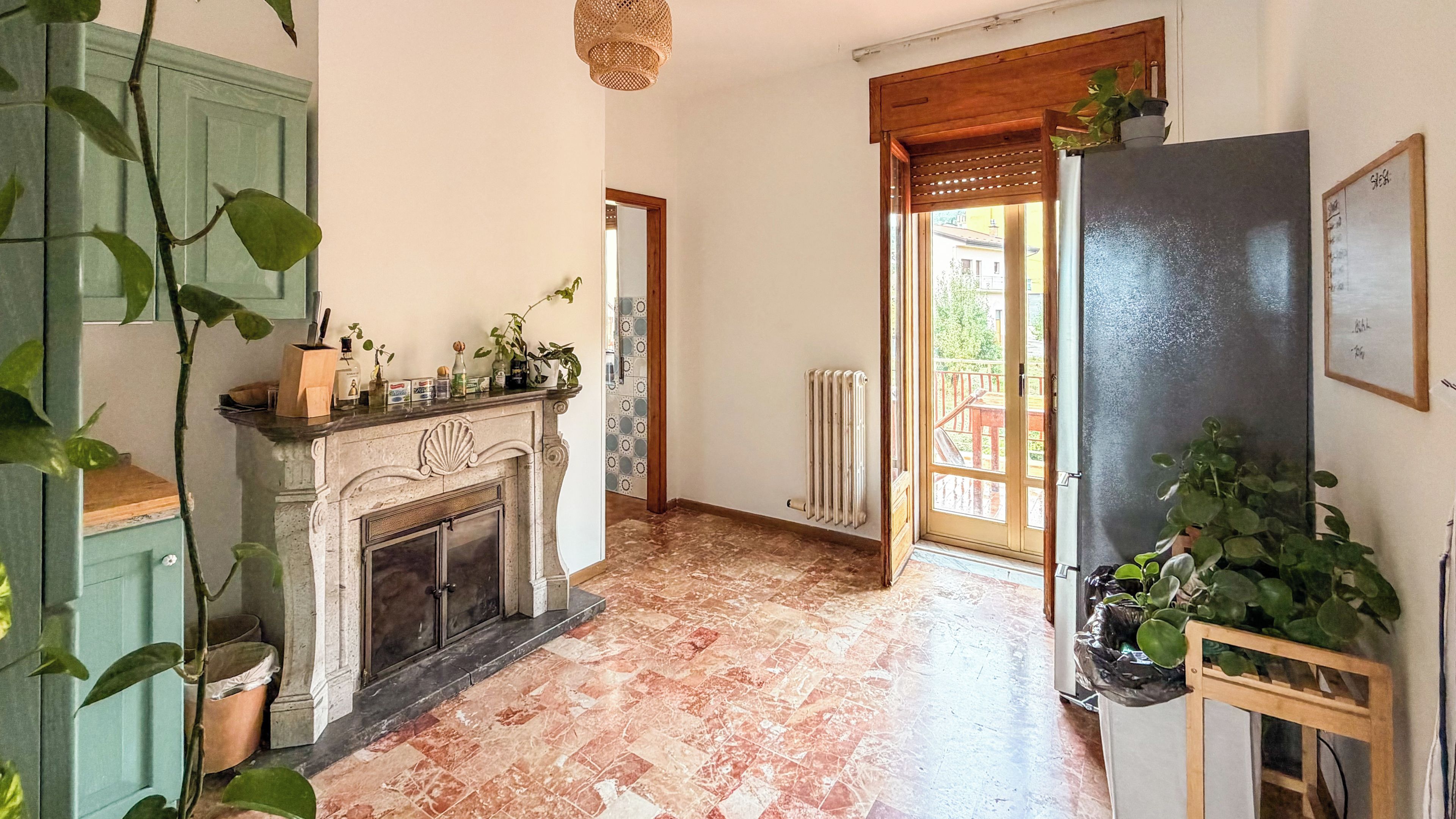 A room with a fireplace, a radiator, a wooden door, and a view of the outside.