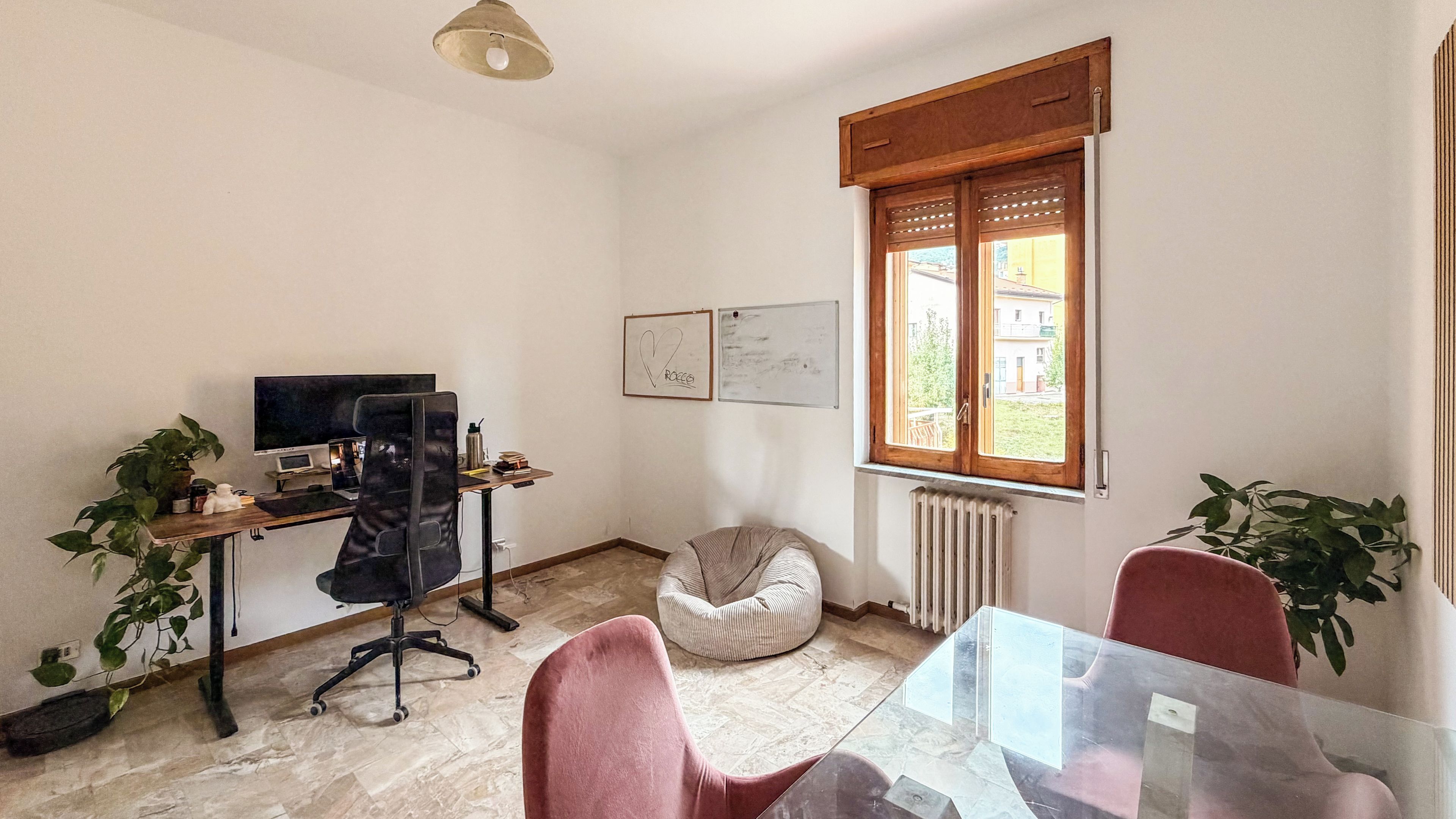 A room with a desk, computer, chair, bean bag, and a table with chairs.