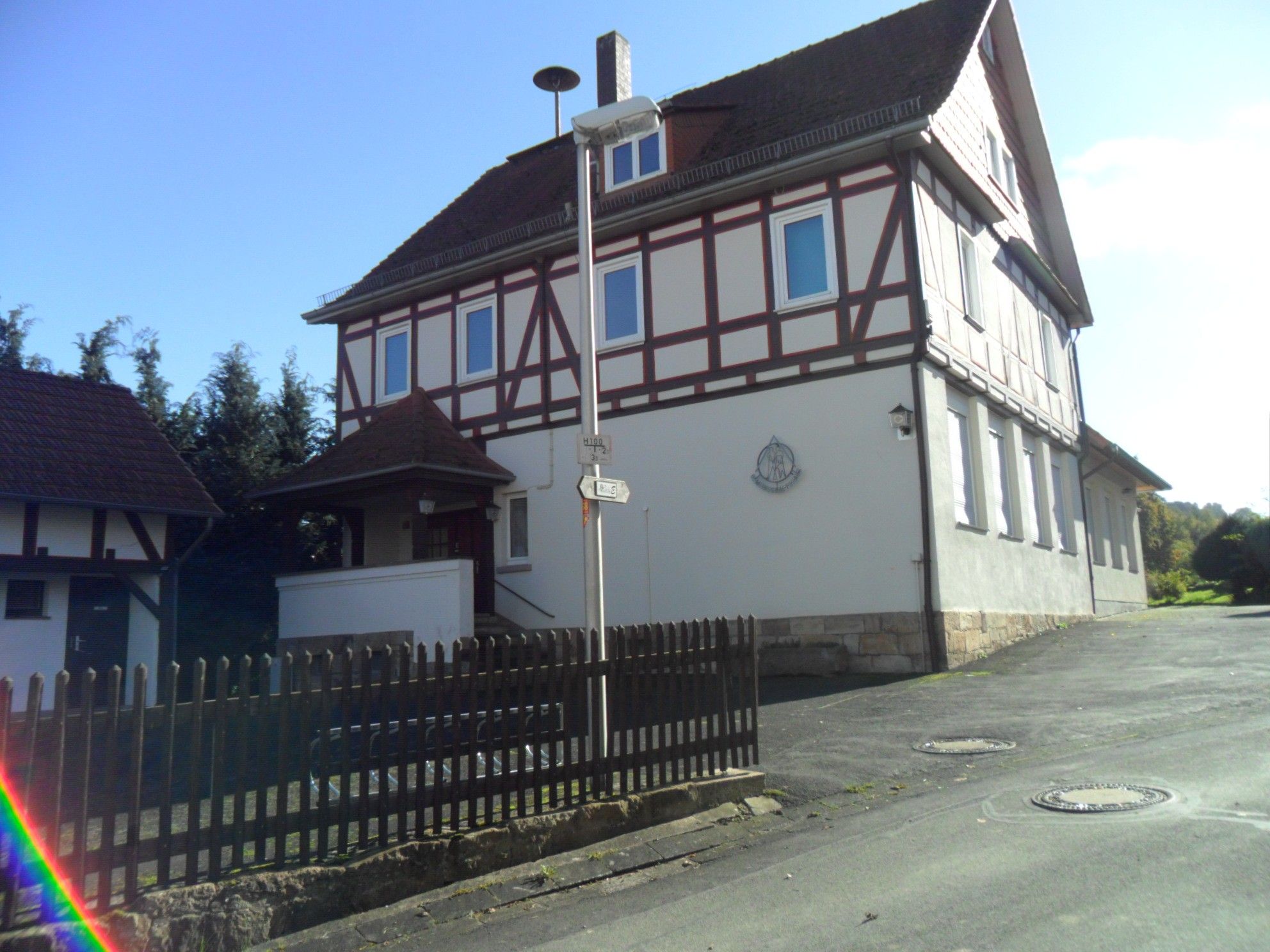 Un bâtiment à deux étages doté d’une façade traditionnelle à colombages, d’une allée d’accès fermée par un portail et d’un ciel dégagé.