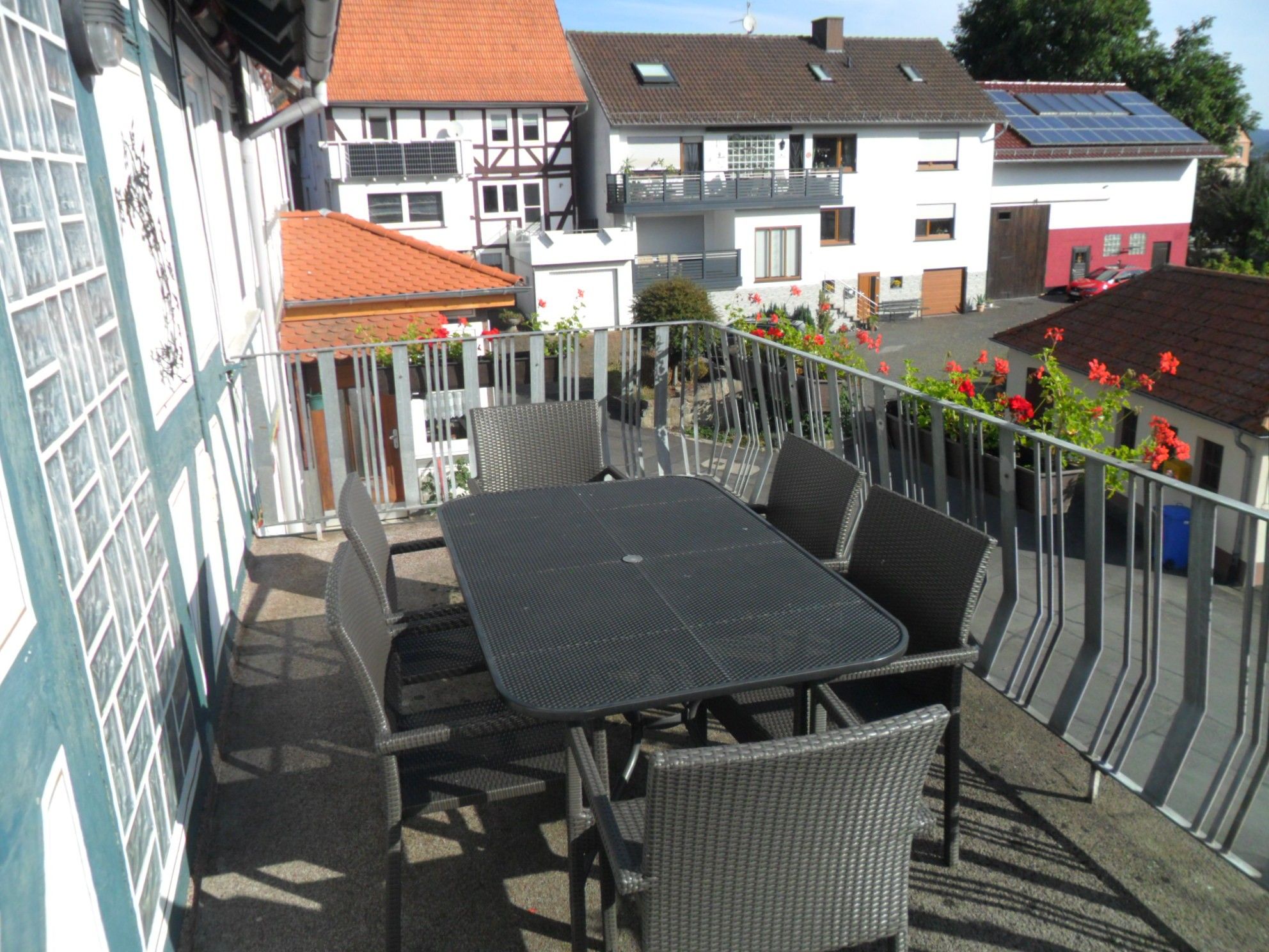 A terrace with a table and chairs, a metal railing, and buildings in the background.