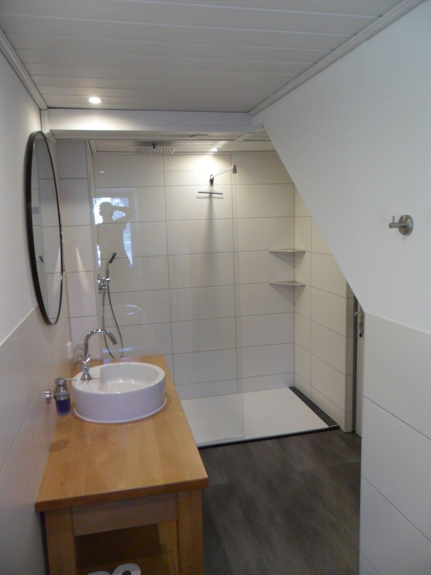 Ein modernes Badezimmer mit einem Holzbadschränkchen, einem weißen Waschbecken und einer Duschkabine.