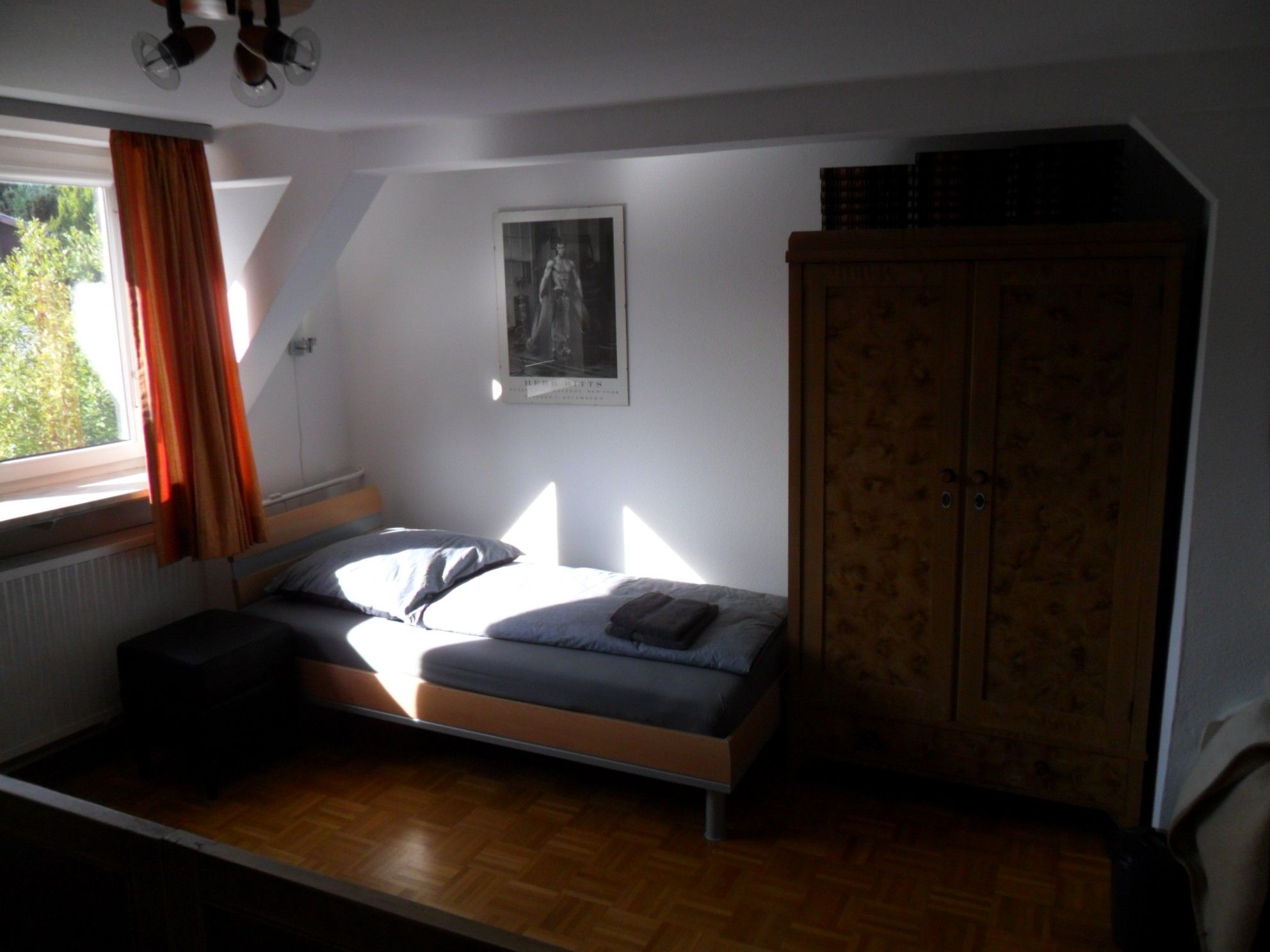 Ein Schlafzimmer mit einem Bett, einem Kleiderschrank, einem Fenster mit Vorhängen und einem Poster an der Wand.