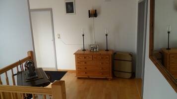 Ein Zimmer mit einem hölzernen Schminktisch, einem Koffer, einem Tisch mit Stuhl und einem Spiegel an der Wand.