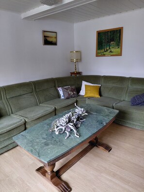 Een woonkamer met een groene hoekbank, een marmeren salontafel en twee schilderijen aan de muur.