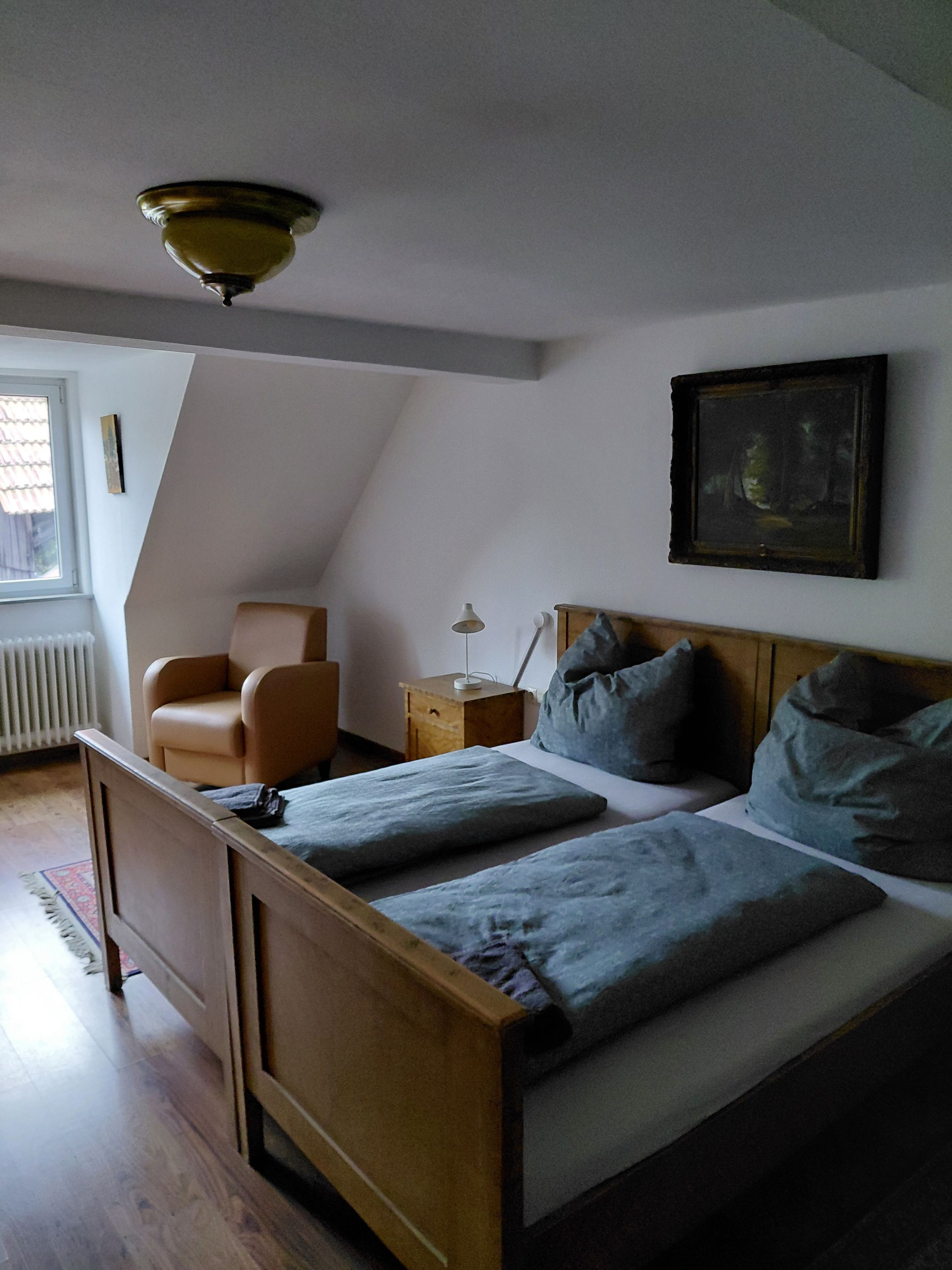 Une chambre à coucher avec un lit en bois, une chaise, une table de chevet, une lampe et un tableau accroché au mur.