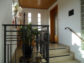 Un escalier avec une rampe en métal, un pot de fleurs et une porte donnant sur une autre pièce.