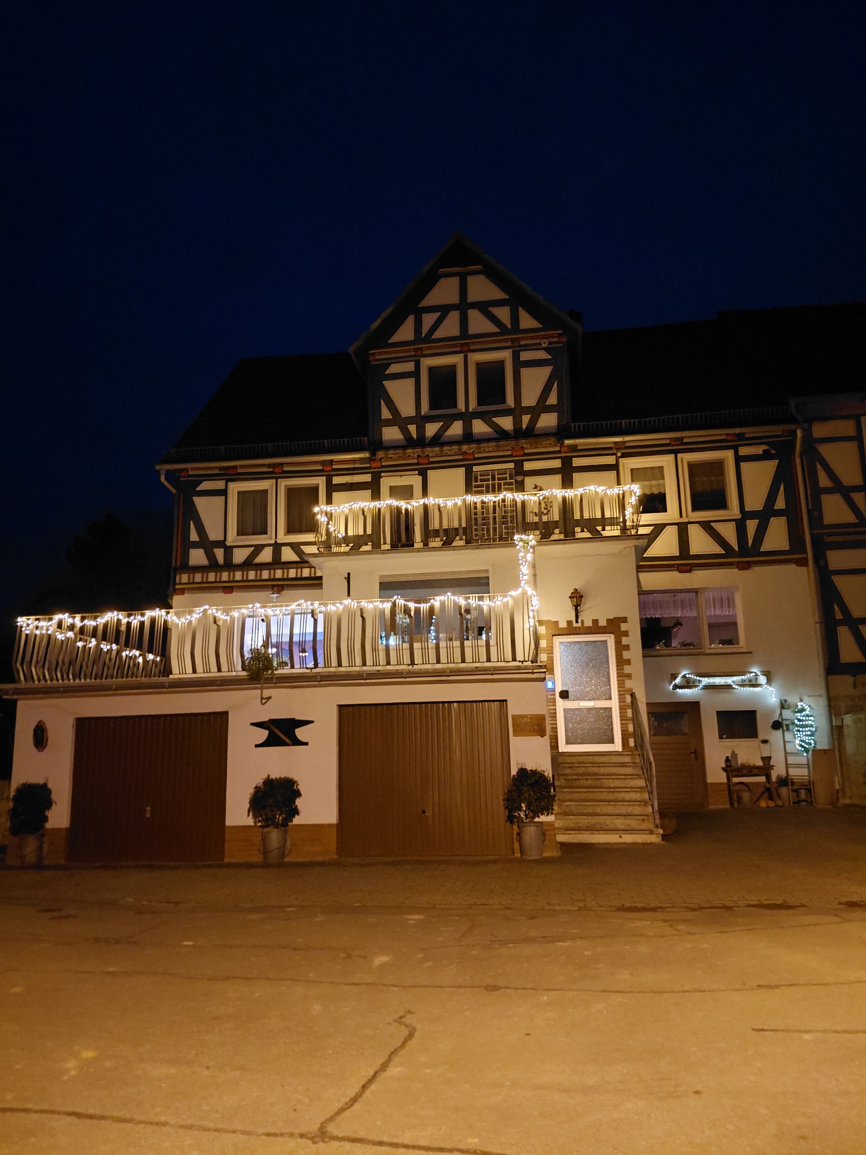 A traditional half-timbered building with a balcony adorned with string lights, a garage, and potted plants.