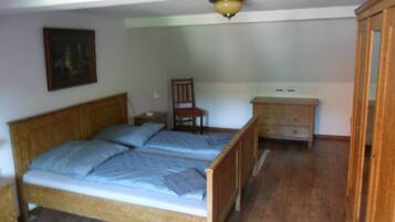 Ein Schlafzimmer mit einem hölzernen Bett, einem Sessel, einem Nachttisch, einer Kommode und einer Deckenleuchte.