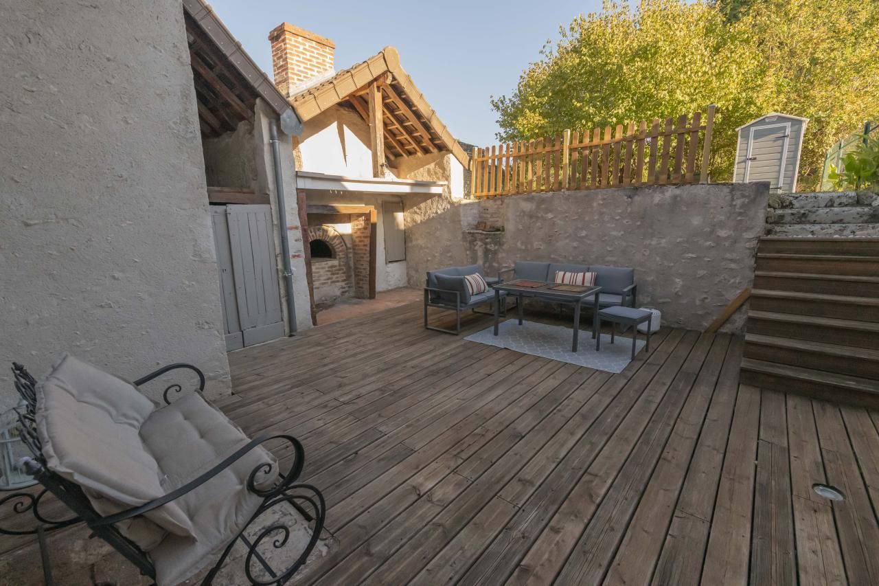 Une terrasse en bois avec des meubles d’extérieur, un mur en pierre et une clôture en bois.