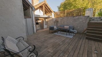 Une terrasse en bois avec des meubles d’extérieur, un mur en pierre et une clôture en bois.