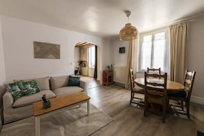Een woonkamer met een bank, een houten salontafel en een eethoek met een tafel en stoelen.