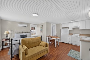 Un espacio habitable compacto con cama, sofá, mesa de comedor, sillas, kitchenette y techo con iluminación empotrada.