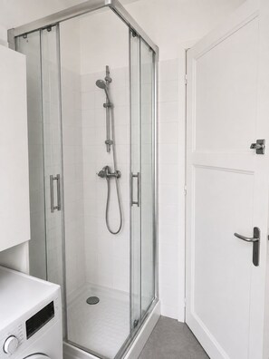 Une salle de bain moderne avec une douche à parois de verre, des carreaux blancs et une porte blanche.