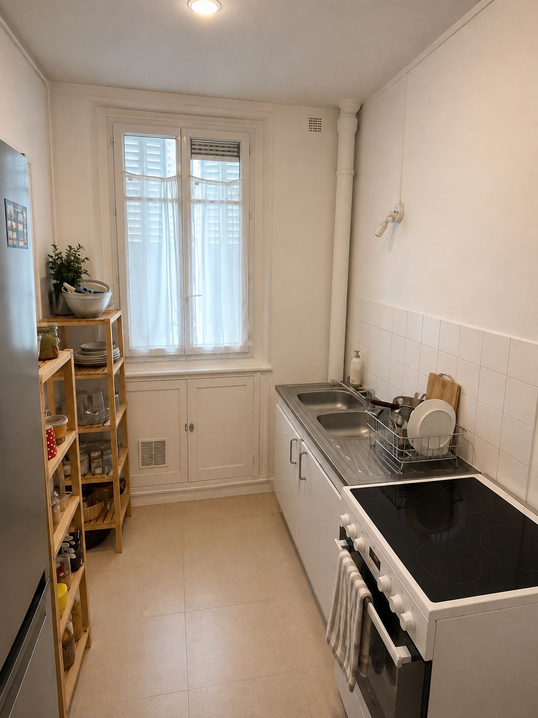 Une cuisine équipée d’une cuisinière, d’un évier et d’une fenêtre. On y trouve des étagères avec de la vaisselle et une plante.