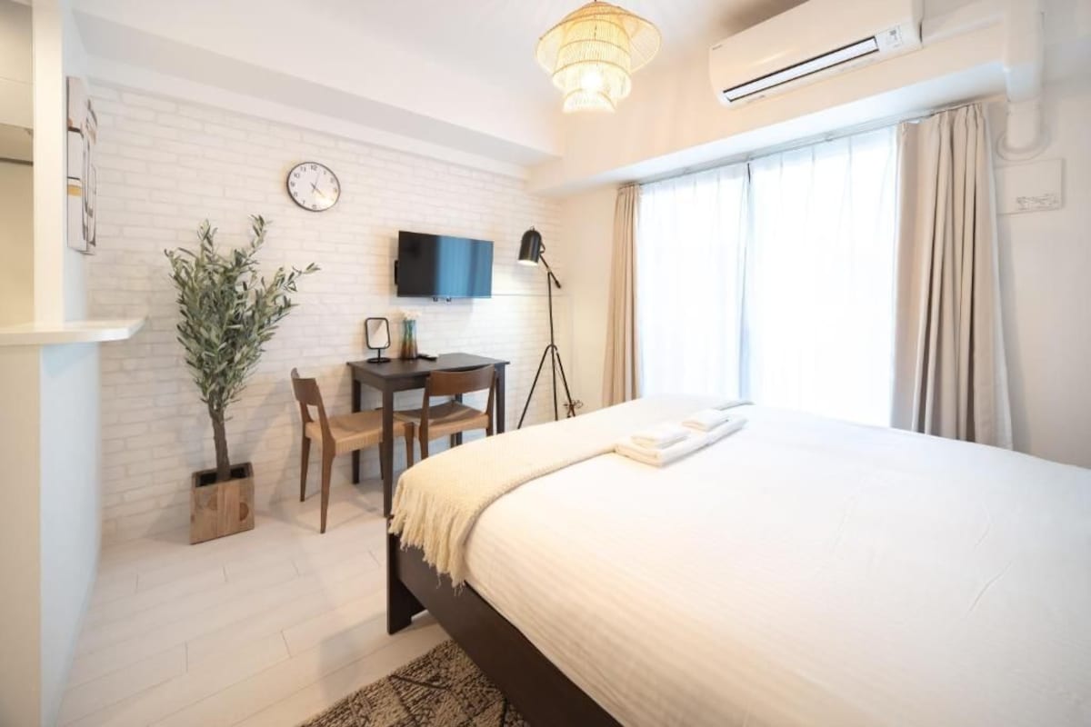 A hotel room with a bed, a desk, a chair, a television, and a potted plant.
