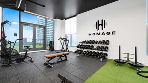 A gym with exercise equipment, a bench, dumbbells, and a logo on the wall. - NEW   High-Rise 1BR Den  Rooftop Pool   Gym 402 (Miami)
