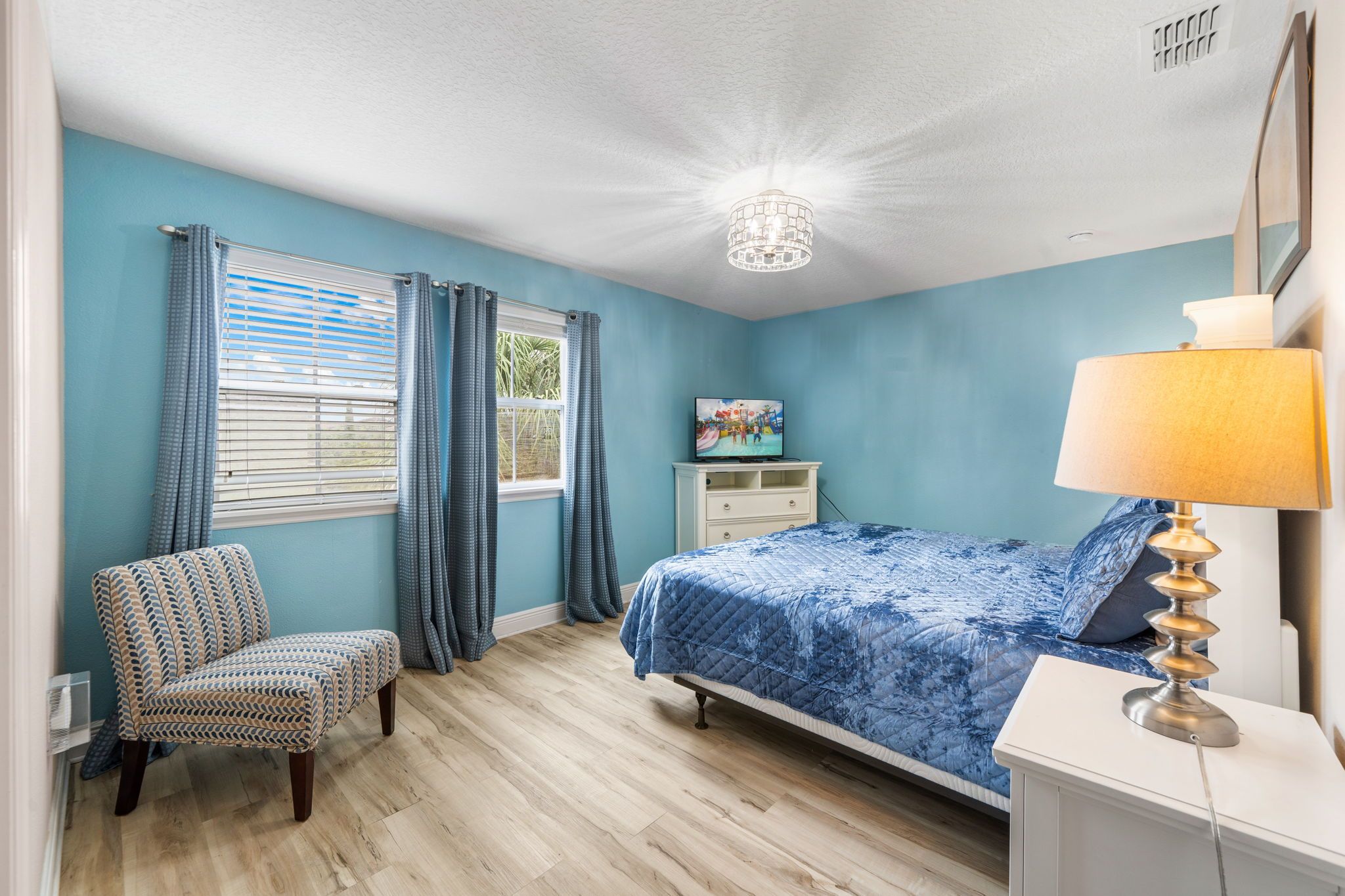A bedroom with a bed, a chair, a dresser, a lamp, and a television.