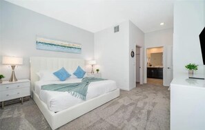 A bedroom with a bed, bedside tables, a nightstand, a painting on the wall, and a door leading to a bathroom. - NEW   2Bd Retreat with Game Room   Lazy River 9333 (Davenport)