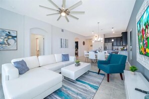 Una sala de estar moderna con un sofá seccional blanco, un sillón azul y un comedor con mesa y sillas blancas.