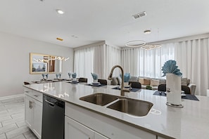 A modern kitchen with a central island, stainless steel appliances, and a dining area with a sofa and curtains. - NEW   4BR Private Pool  Lazy River   Themed Rooms (Kissimmee)