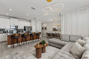 A modern kitchen with stainless steel appliances, a dining area with bar stools, and a living room with a grey sofa. - NEW   4BR Private Pool  Lazy River   Themed Rooms (Kissimmee)